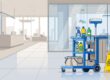 Cleaning supplies and a caution cone sit beside a clear office lobby walkway.