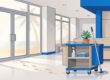 A cleaning cart with reusable supplies sits beside a sunny office entrance.