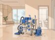 A cleaning cart stands in a bright lobby with polished floors and glass doors.